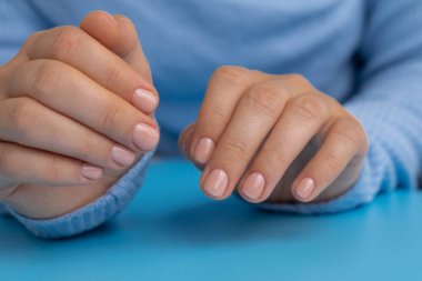 Pastel yumuşaklığı mavi arka planda manikürlü tırnaklar. Pastel paletin renginde yeni manikürünü gösteren bir kadın. Basitlik dekoru Taze bahar titreşimleri Toprak renginde nötr tonlar tasarım