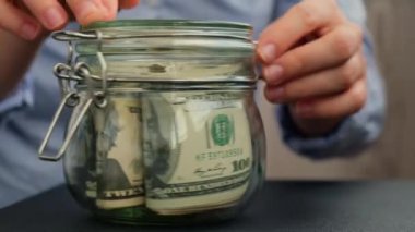 Kadın eli, cam kavanozu Amerikan dolarlarıyla doldurur. Nakit para. Metin eğitimiyle. Hazırlık para tasarrufu. Orta karar tüketim ve ekonomi. Para toplama