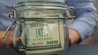 Tanınmayan bir kadın para biriktirme kavanozunu dolar banknotlarıyla doldurdu. Bebek transkripti kavanozun önünde. Kişisel finansman yönetimi gelecek için ekstra gelir