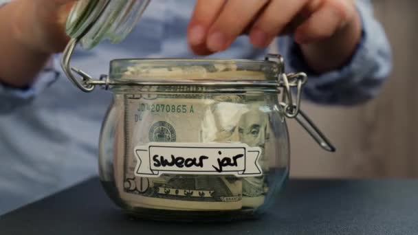 女性の手は Swear Jarテキストでアメリカの通貨ドル紙幣でいっぱいのガラス瓶からお金を取ります お金を節約する準備 適度な消費と経済 お金の収集について — ストック動画