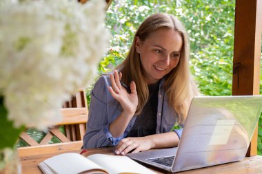 Çevrimiçi olarak çalışan genç bir kadın dizüstü bilgisayar kullanıyor ve bahçedeki güzel doğanın tadını çıkarıyor. Çevrimiçi buluşma eğitimi. Çalışma, tatilden çalışma, melez iş modeli