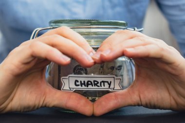 Kadın kalp işareti gösteriyor. Dolarla dolu cam kavanozda para biriktiriyor. Kavanozun önünde CHARITY kopyası. Gelecekteki güvensizlik geçmişi için kişisel finansman yöneticiliği