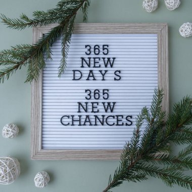 365 NEW GÜN 365 NEW CHANCES beyaz harfli yazı tahtasında yeşil arka planda Noel dekoru ile. Yeni yıl kararları hedefler. Yeni yıl konsepti