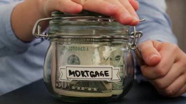 Kadın eller, Amerikan dolarlarıyla dolu cam kavanozdan para alıyor. Morgage yazılı nakit para. Hazırlık para tasarrufu. Orta karar tüketim ve ekonomi. Para toplama