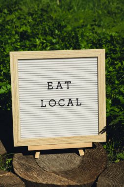 EAT LOCAL message on background of fresh eco-friendly bio grown green herb parsley in garden. Countryside food production concept. Locally produce harvesting. Sustainability and responsibility  clipart