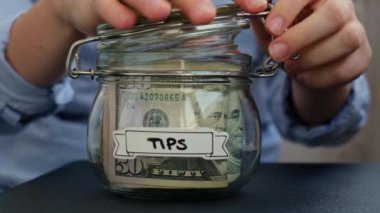 Tanınmayan bir kadın, Amerikan dolarlarıyla dolu cam kavanozdan TIPS 'li nakit para alıyor. Tasarruf için hazırlık yapın. Orta karar tüketim ve ekonomi. Para toplama