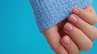 Manikürlü kadınlar, şık bej tırnaklar. Mavi arka planda mavi süveterli kadın elinin manikürlü tırnakları. Kış ya da sonbahar tırnak tasarımı konsepti. Güzellik tedavisi.