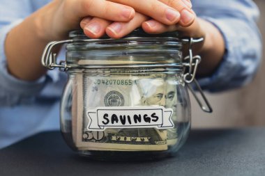 Dolarla dolu cam kavanozda para biriktiren tanınmamış bir kadın. Tasarruf metni kavanozun önünde. Gelecekteki güvensizlik geçmişi için kişisel finansman yöneticiliği