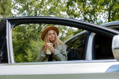 Tekrar kullanılabilir termostan kahve ya da çay içen gülümseyen genç bir kadın. Gezgin hafta sonları yerel solo seyahat konseptinde kahve molası veriyor. Çıkan kadın ormanda özgürlüğü keşfediyor. Birlik