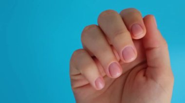 Pastel yumuşaklığı mavi arka planda manikürlü tırnaklar. Pastel paletin renginde yeni manikürünü gösteren bir kadın. Basitlik dekoru Taze bahar titreşimleri Toprak renginde nötr tonlar tasarım