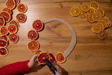 Kurutulmuş portakallı greyfurt dilimlerinden el yapımı Noel çelengi. Tatil hazırlığı, yaratıcı dekorasyon ustası sınıfı. Elle yapılan etkinlikler, sürdürülebilir sorumlu tatil hediyesi atölyesi yaratımı. Üst manzara, düz uzanma