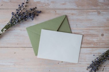 Beyaz kağıttan tebrik kartının düz kompozisyonu kuru lavanta çiçekleriyle dolu zarfın üzerindeydi. Uzay şablonunu kopyala. Üst Manzara. Düğün davetiyesi kartpostalı konsepti. Ticari reklam markası