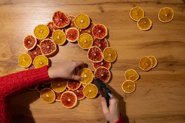 Kuru meyve portakalları ve greyfurtlardan yapılmış el yapımı Noel çelengi kullanan kadının adım adım talimatı. Kadın elleri el yapımı dekorasyon yapıyor. Yeni yıl kutlaması. Kış tatili
