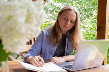 Young happy woman focuses on her laptop in wooden alcove. Relaxed outdoor setting emphasizes comfort and productivity. Remote work learning concept clipart