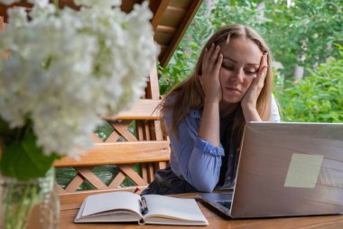 Depresyondaki genç mutlu kadın, ahşap oyuktaki dizüstü bilgisayarına odaklanıyor. Uzak çalışma öğrenme kavramı zorlukları. Dezavantajlar ve olumsuz yönler profesyonel tükeniş
