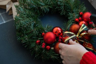 Dekoratif kurdele Basamağı 'nı bağlayan kadın adım adım kırmızı renklerle süslenmiş el yapımı Noel çelengi yapıyor. Kadın elleri el yapımı dekorasyon yapıyor. Yeni yıl kutlaması