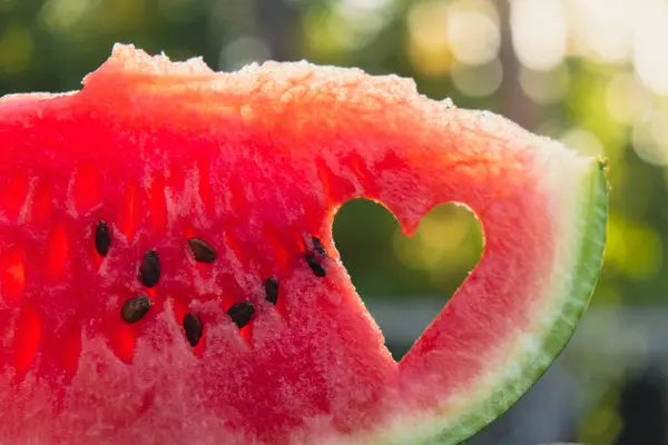 stock image Fresh juicy red watermelon heart shaped slice in hands on background of outdoor garden in summertime during sunset. Concept of love happiness summer holidays and vacation. Slow-living simple pleasures