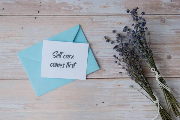 stock image SELF CARE COMES FIRST text on supportive message paper note reminder from blue envelope. Flat lay composition dry lavender flowers. Concept of inner happiness, slowing-down digital detox personal