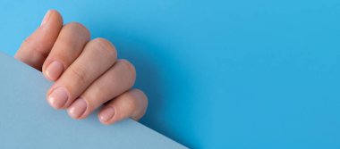 Manikürlü kadınlar, şık bej tırnaklar. Mavi arka planda mavi süveterli kadın elinin manikürlü tırnakları. Şablon kopyalama alanı Kış veya tırnak tasarımı konseptinin sonbahar stili