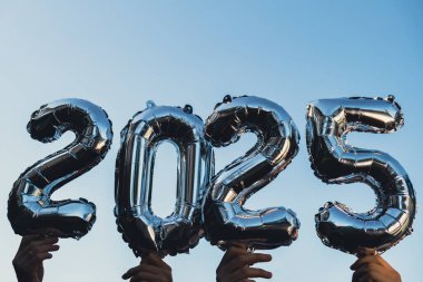 2025 numaralı gümüş folyo mavi gökyüzü arka planında yeni yıl balonunu kutluyor. Mutlu yıllar konsepti. İki bin yirmi dört yıllık Noel tatili konsepti. 