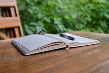 Bahçedeki ahşap masada boş beyaz kağıt defter. Kişisel yansıma günlüğü kavramı, şükran günlüğü yazma