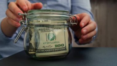 Kadın eli, cam kavanozu Amerikan dolarlarıyla doldurur. Vergi ile nakit para. Hazırlık para tasarrufu. Orta karar tüketim ve ekonomi. Para toplama