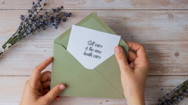 Yeşil zarfın içindeki yeni sağlık bakımı, kağıt kâğıt kağıtları ve SELF özenle alan kadın elidir. Lavanta çiçeği. Üst manzara, düz yatış. Ruhsal sağlık hizmeti kavramı.