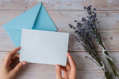 Beyaz kağıttan tebrik kartının düz kompozisyonu kuru lavanta çiçekleriyle dolu zarfın üzerindeydi. Uzay şablonunu kopyala. Üst Manzara. Düğün davetiyesi kartpostalı konsepti. Ticari reklam markası