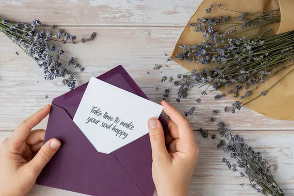 stock image Female hands taking paper card note with text TAKE TIME TO MAKE YOUR SOUL HAPPY from violet envelope. Lavender flower. Top view, flat lay. Concept of mental spiritual health self care wellbeing