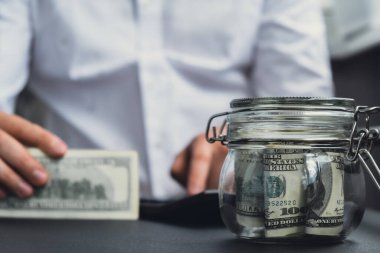 Adam hesap makinesinde masraf banknotlarını sayıyor. Tanınmayan bir iş adamının eli kulağında. Bütçe yatırımı kavramını sakla. Amerikan doları tasarruf fonu kavramı