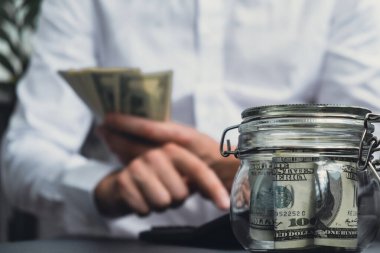 Dolar banknotu cam kavanozda para biriktiriyor. Tanınmayan adam, Orta Yol Tüketim ve Ekonomi Biriktirme İşletme Finansmanı kavramında para hesapladı