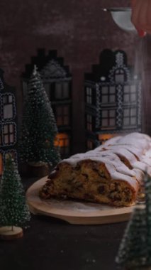 Noel ışıkları ve dekorasyonunda düşen şeker tozuyla Noel Stollen dikey görüntüsü. Geleneksel meyveli somun şekerli, şenlikli tatlı. Tatil pişirme konsepti. 