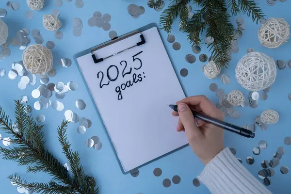 Stock image Female hands writing handwritten 2025 GOALS new year resolutions aims goals on paper notepad. Preparation for New Year. Concept of planning and setting goals for personal development 