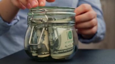 Kadın eli, Amerikan dolarlarıyla dolu kavanozu SWEAR JAR mesajıyla doldurur. Hazırlık para tasarrufu. Orta karar tüketim ve ekonomi. Para toplama