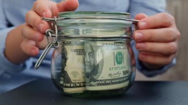 Tanınmayan bir kadın para biriktirme kavanozunu dolar banknotlarıyla doldurdu. Emekli transkripti kavanozun önünde. Gelecekteki güvensizlik geçmişi için kişisel finansman yöneticiliği