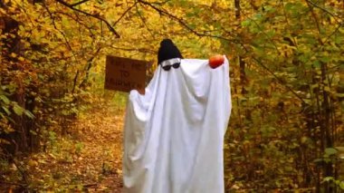 Sonbahar zamanı dışarıda moda cadılar bayramı kutlaması. Çarşaflardan, şapkadan ve gözlüklerden yapılmış el yapımı hayalet dans kostümü. Sonbahar ormanı portakal yaprakları. 