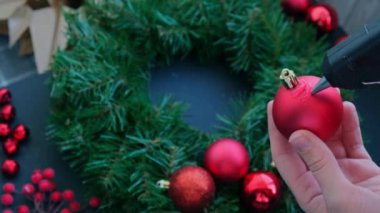 Şenlikli kırmızı süslemelerden elde yapılmış el yapımı Noel çelengi kullanan el sanatları ustası. Tatil hazırlığı, yaratıcı dekorasyon ustası sınıfı. Etkin faaliyetler sürdürülebilir sorumluluk