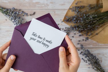 Female hands taking paper card note with text TAKE TIME TO MAKE YOUR SOUL HAPPY from violet envelope. Lavender flower. Top view, flat lay. Concept of mental spiritual health self care wellbeing clipart