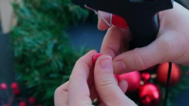 Şenlikli kırmızı süslemelerden elde yapılmış el yapımı Noel çelengi kullanan el sanatları ustası. Tatil hazırlığı, yaratıcı dekorasyon ustası sınıfı. Etkin faaliyetler sürdürülebilir sorumluluk