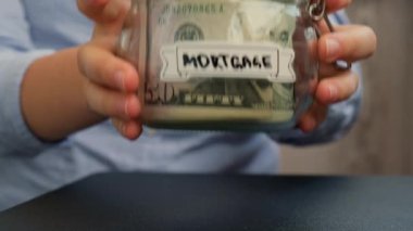 Kadın elleri, cam kavanozun üzerine Amerikan doları dolu nakit banknot ile Morgage metni konuldu. Hazırlık para tasarrufu. Orta karar tüketim ve ekonomi. Para toplama