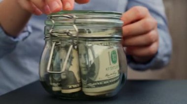 Kadın eli, Amerikan dolarlarıyla dolu kavanozu SWEAR JAR mesajıyla doldurur. Hazırlık para tasarrufu. Orta karar tüketim ve ekonomi. Para toplama