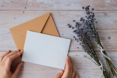 Beyaz kağıttan tebrik kartının düz kompozisyonu kuru lavanta çiçekleriyle dolu zarfın üzerindeydi. Uzay şablonunu kopyala. Üst Manzara. Düğün davetiyesi kartpostalı konsepti. Ticari reklam markası