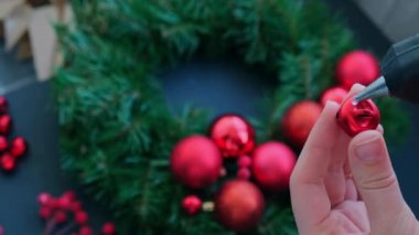 El sanatları ustası, bir kadının kırmızı dekorlu Noel düzenlemesi için sıcak yapıştırıcı kullanıyor. Küçük işletme, serbest meslek sahibi girişimci, kendi kendini yetiştirmiş bir kariyer. El yapımı zanaat talimatları serisi