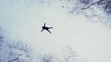Adam uzanmış, kar meleği yapıyor. Açık hava aktiviteleri ve ekolojik turizm. Doğal kış mevsimi geçmişi. İHA 'nın karını kaplayan çam ağacının havadan görünüşü