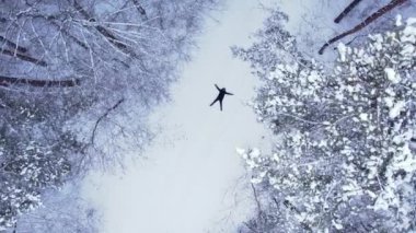 Adam uzanmış, kar meleği yapıyor. Açık hava aktiviteleri ve ekolojik turizm. Doğal kış mevsimi geçmişi. İHA 'nın karını kaplayan çam ağacının havadan görünüşü