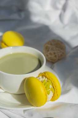 Tatlı sarı Makaron Tatlı Fincanı yeşil bitki bazlı kibrit çaylı latte, rahat bir sabah yatağı atmosferinde. Yaratıcı tatil romantik randevu fikri. Bitkisel prebiyotik fiber süper yiyecek. Antioksidan zengini.