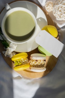 Boş mesaj kâğıdı fotokopisi: Besin zengini kibrit içeceği, ahşap tepside taze çiçeklerle süslü, modaya uygun makarna tatlısı. Günaydın güzel kahvaltı hediyesi fikri. Canlı, yaratıcı.