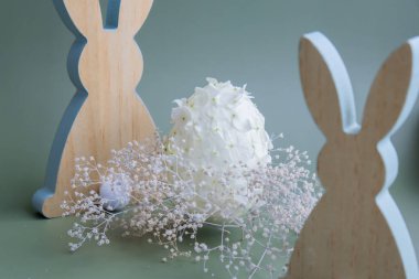 Ahşap minimalizm gösterişsiz tavşan dekoru. Pastel yeşil arka planda beyaz leylak bahar çiçeklerinden yapılmış Paskalya yumurtası. Sürdürülebilir tatil minimalist natüralistik yaşam kompozisyonu. Boşluk şablonunu buraya kopyala