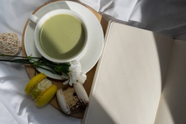 Beyaz sayfalar dolusu defter fotokopi alanı. Sıcak bir sabah yatağında yeşil bitki bazlı kibrit çaylı latte tatlı sarı makarna tatlısı. Yaratıcı tatil romantik randevu fikri. Bitkisel prebiyotik lif