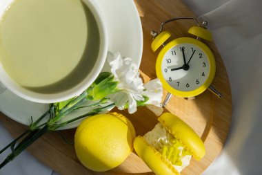 Sarı alarmlı saat konsepti besin zengini kibrit çayı ile uyanmak ahşap tepside taze çiçeklerle son moda makaron tatlısı. Günaydın güzel kahvaltı hediyesi fikri. Canlı, yaratıcı.